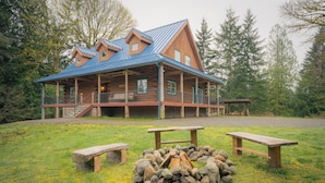 A log cabin with a metal roof, a porch, and a fire pit area. - Blue Roof Lodge - Forest Getaway for Groups (Enumclaw)