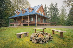 A log cabin with a metal roof, a porch, and a fire pit area. - Blue Roof Lodge - Forest Getaway for Groups (Enumclaw)