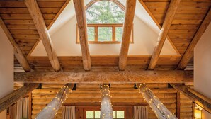 A log cabin interior with exposed wooden beams, a triangular window, and string lights. - Blue Roof Lodge - Forest Getaway for Groups (Enumclaw)