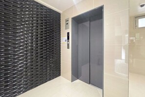 A modern elevator with a metallic finish, a wall with a textured pattern, and a tiled floor. - BLUE Simanouchi (Osaka)