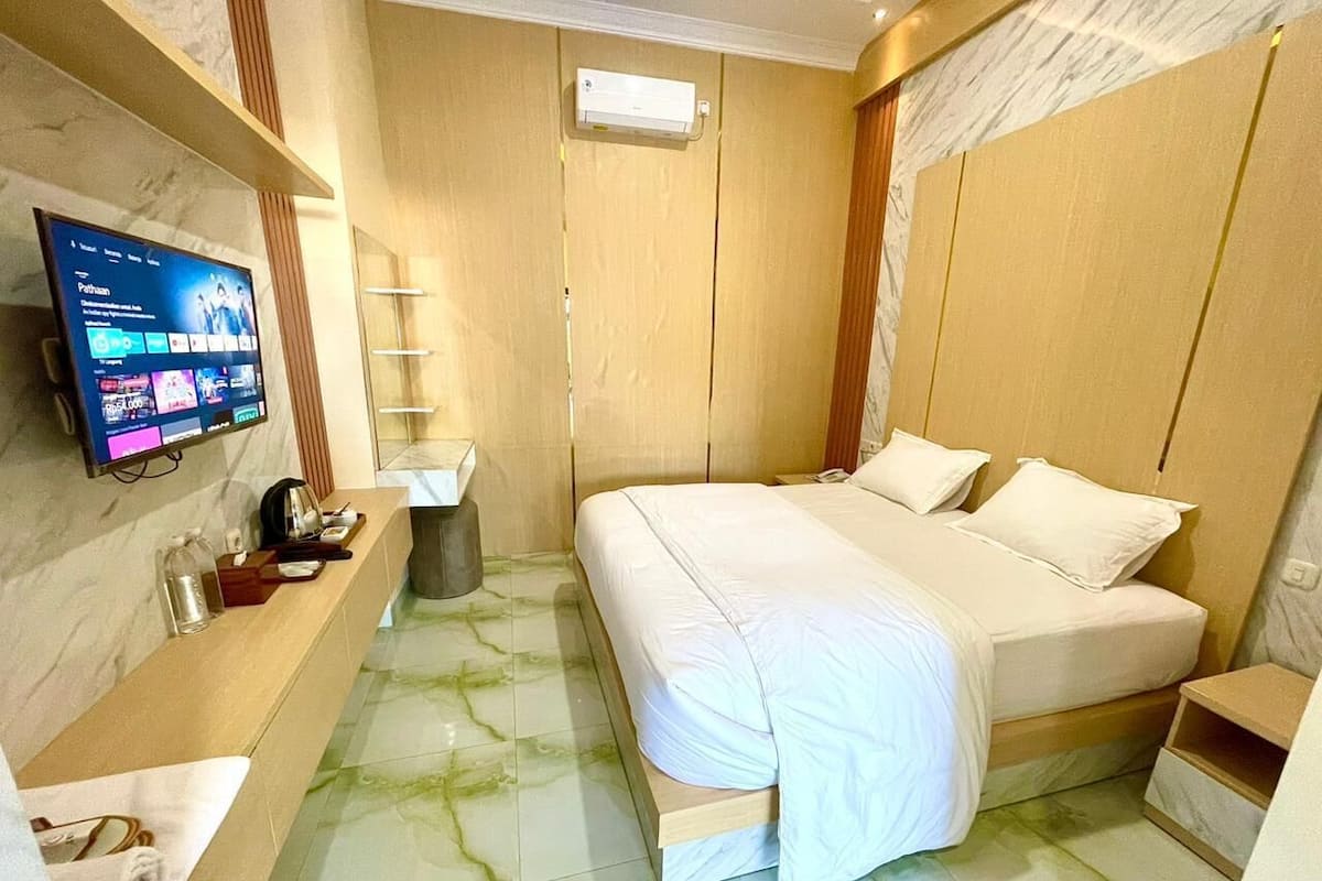 A hotel room with a bed, a TV, a vanity with a mirror, and a bathroom.
