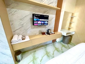 A modern bathroom with a marble vanity, a mounted TV, a towel rack, and a sink. - Alzetta Hotel by Abiza (Yogyakarta)
