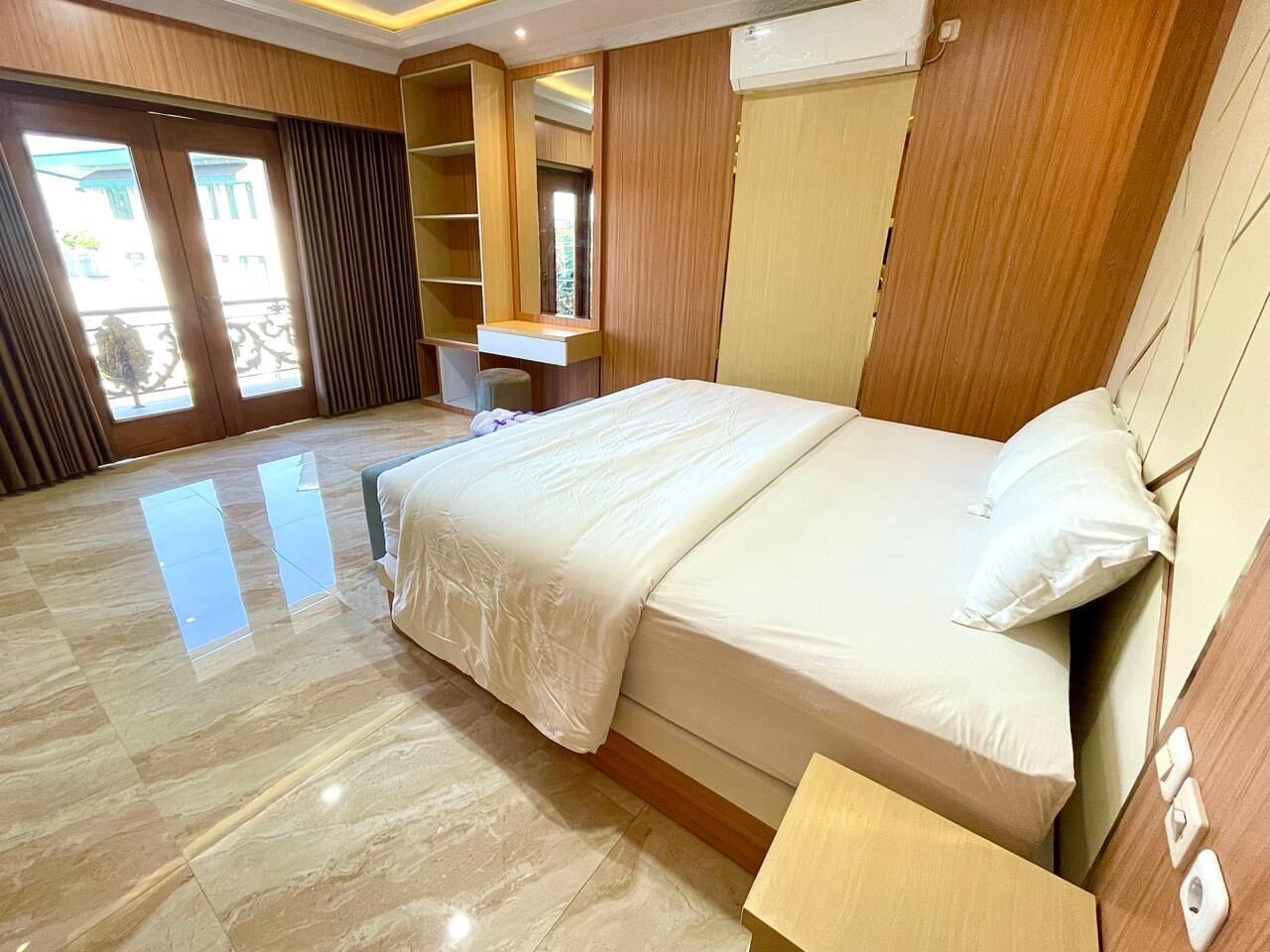 A hotel room with a large bed, a desk, a mirror, and a wardrobe.