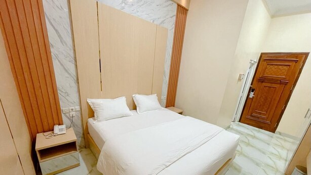 A hotel room with a bed, a nightstand, a wooden wardrobe, and a door. - Alzetta Hotel by Abiza (Yogyakarta)