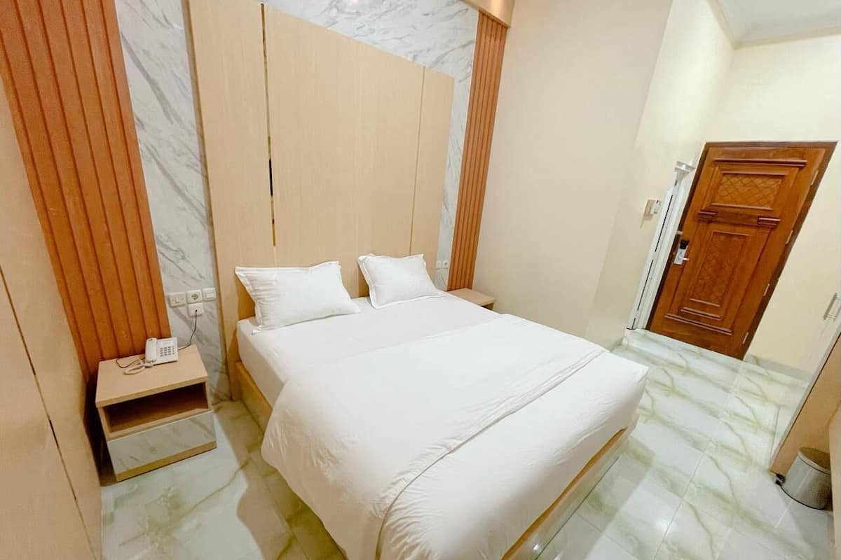 A hotel room with a bed, a nightstand, a wooden wardrobe, and a door.