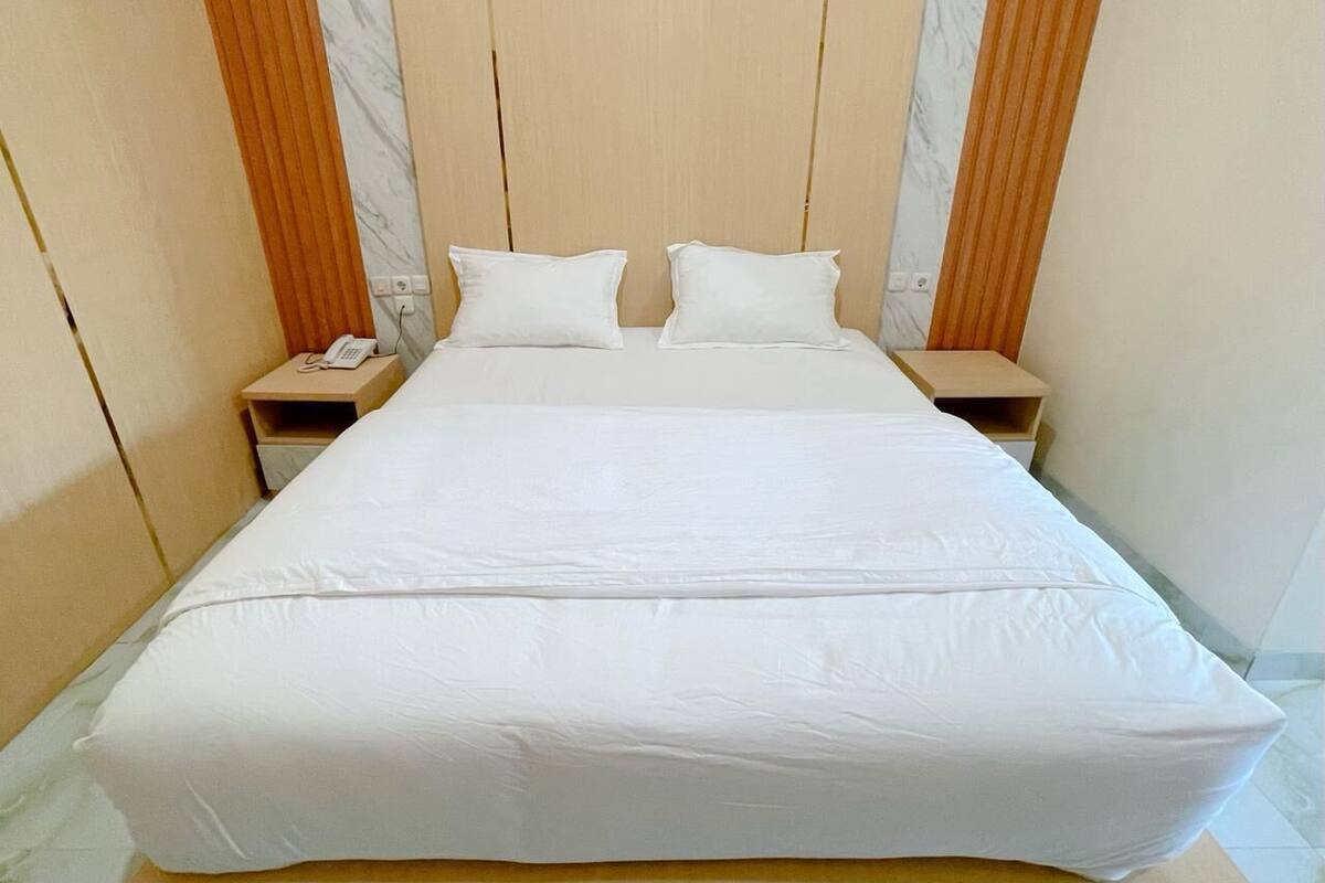 A bed with white linens, two nightstands, and a wooden headboard.