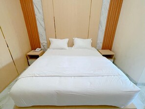 Una cama con sábanas blancas, dos mesitas de noche y un cabecero de madera.