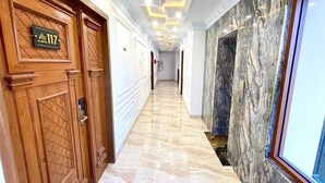A hallway with wooden doors, a marble floor, and a wall with a marble-like texture. - Alzetta Hotel by Abiza (Yogyakarta)