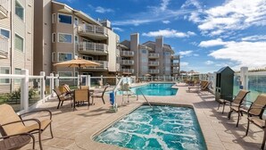 A pool area with lounge chairs and a hot tub, surrounded by multi-story buildings with balconies. - Ocean Shores | Couple Coastal Retreat | Pool | 1BR (Ocean Shores)