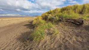 A sandy beach with grass and a log. - Ocean Shores | Couple Coastal Retreat | Pool | 1BR (Ocean Shores)