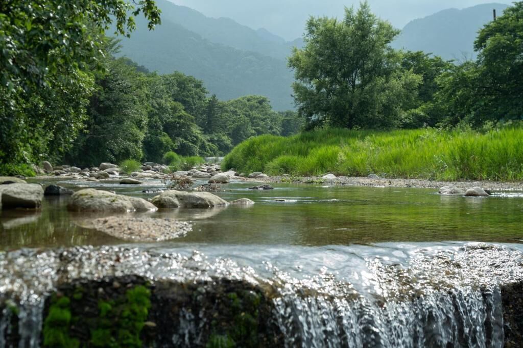 A natural landscape with a flowing river, rocks, and greenery.