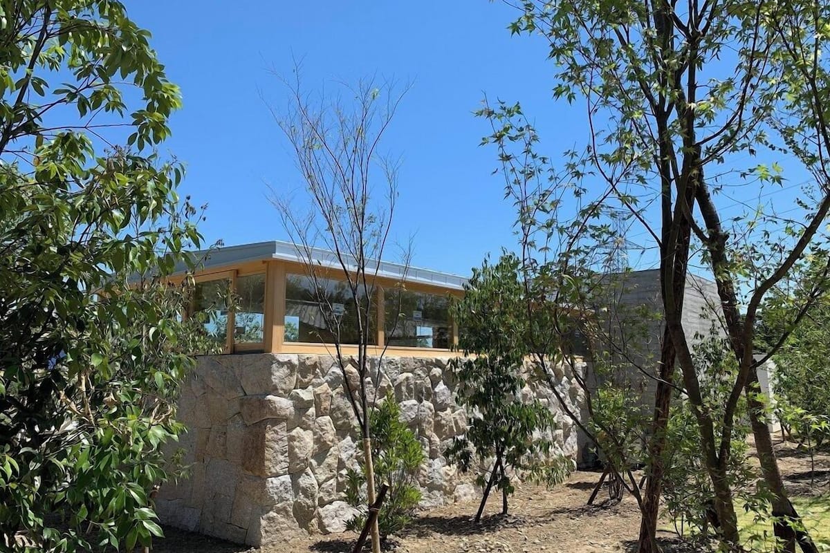 A stone structure with a glass enclosure, surrounded by trees and a clear sky.