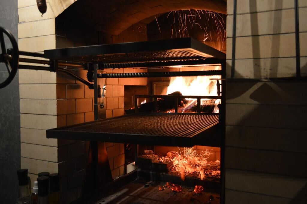Un horno de ladrillo con una rejilla metálica en su interior, llamas visibles y una pared de ladrillo.