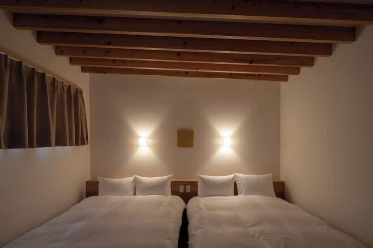 A double room with two beds, wooden ceiling beams, and wall-mounted lights.