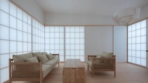 Una habitación minimalista con sofá, dos sillones, una mesa de centro de madera y amplios paneles shoji.