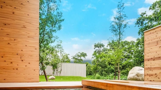 Una terraza de madera con piscina, rodeada de follaje y árboles.