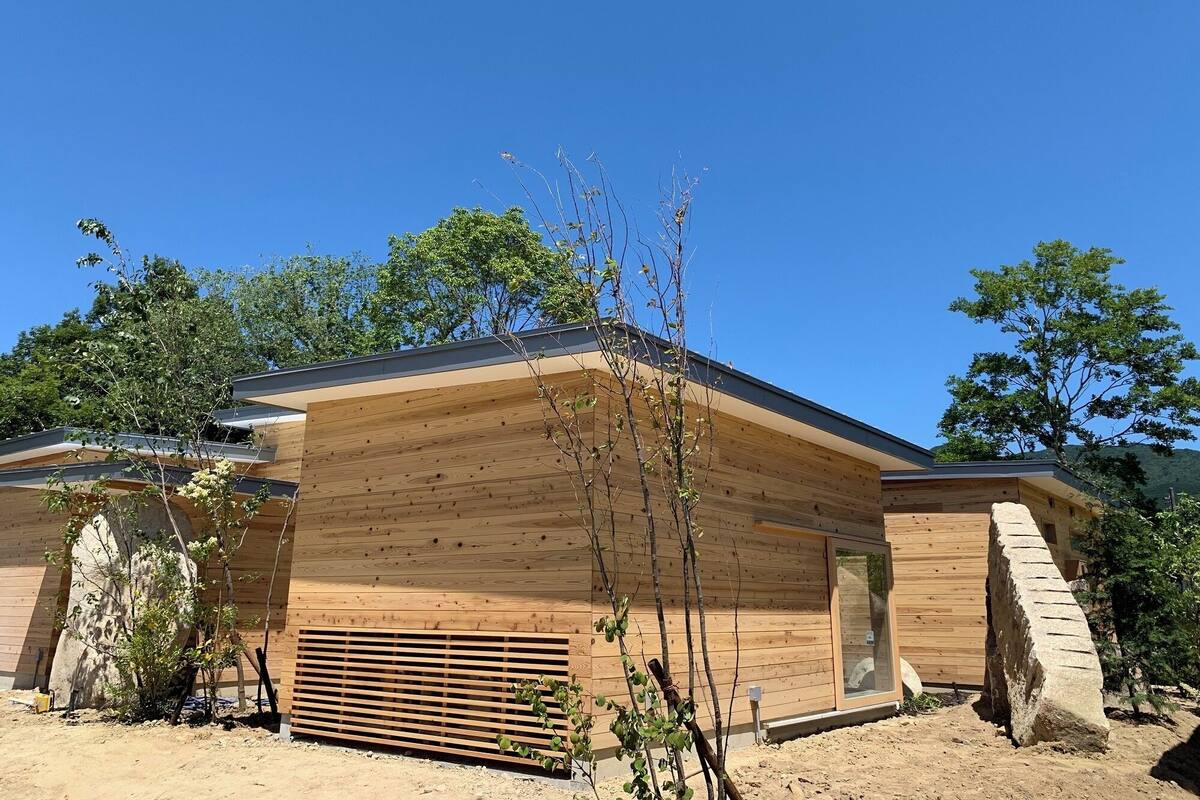 A modern wooden building with a sloped roof, a large window, and a door.