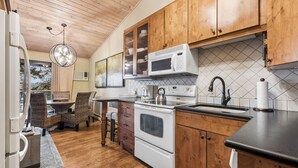 A kitchen with wooden cabinets, a microwave, stove, and a dining area with wicker chairs. - New Listing! Whitefish Lake Condo, 16B, Hillside! (Whitefish)