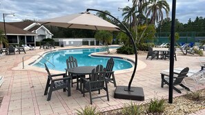 Ein Poolbereich mit Tisch und Stühlen, einer überdachten Sitzgelegenheit und einem Pool mit einer Fliesenbordatur.