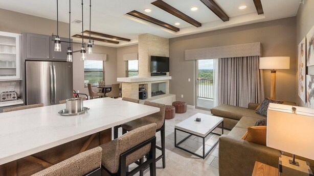 Una cocina moderna con una isla central, zona de comedor con sillas, un sofá y una televisión.