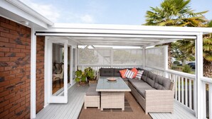 Un patio exterior cubierto con un sofá modular, una mesita y macetas con plantas.