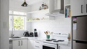 Una cocina moderna con armarios blancos, estufa, lavamanos y cafetera.