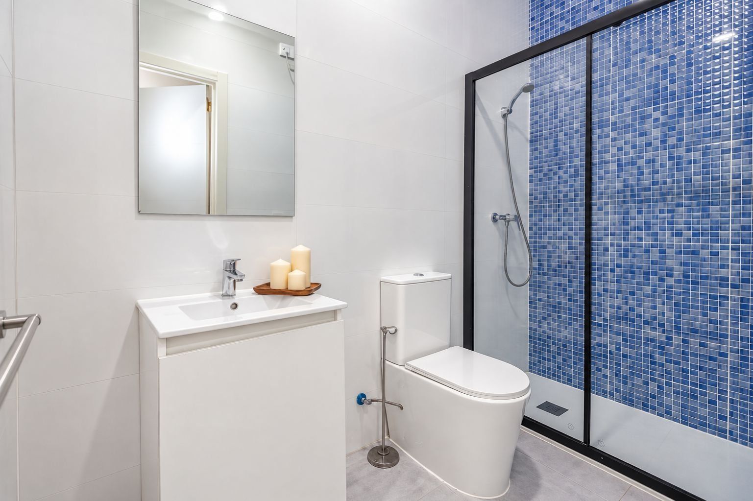 Un bagno moderno con un lavandino bianco, un water e una doccia rivestita di mosaici blu.