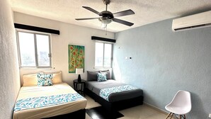 Un dormitorio con dos camas, ventilador de techo, aire acondicionado y ventana.