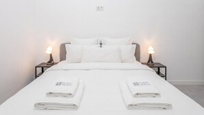 A double bed with white bedding, two bedside lamps, and two folded towels with 'GUEST READY' text. - GuestReady - Cosy studio in Malaga centre (Málaga)