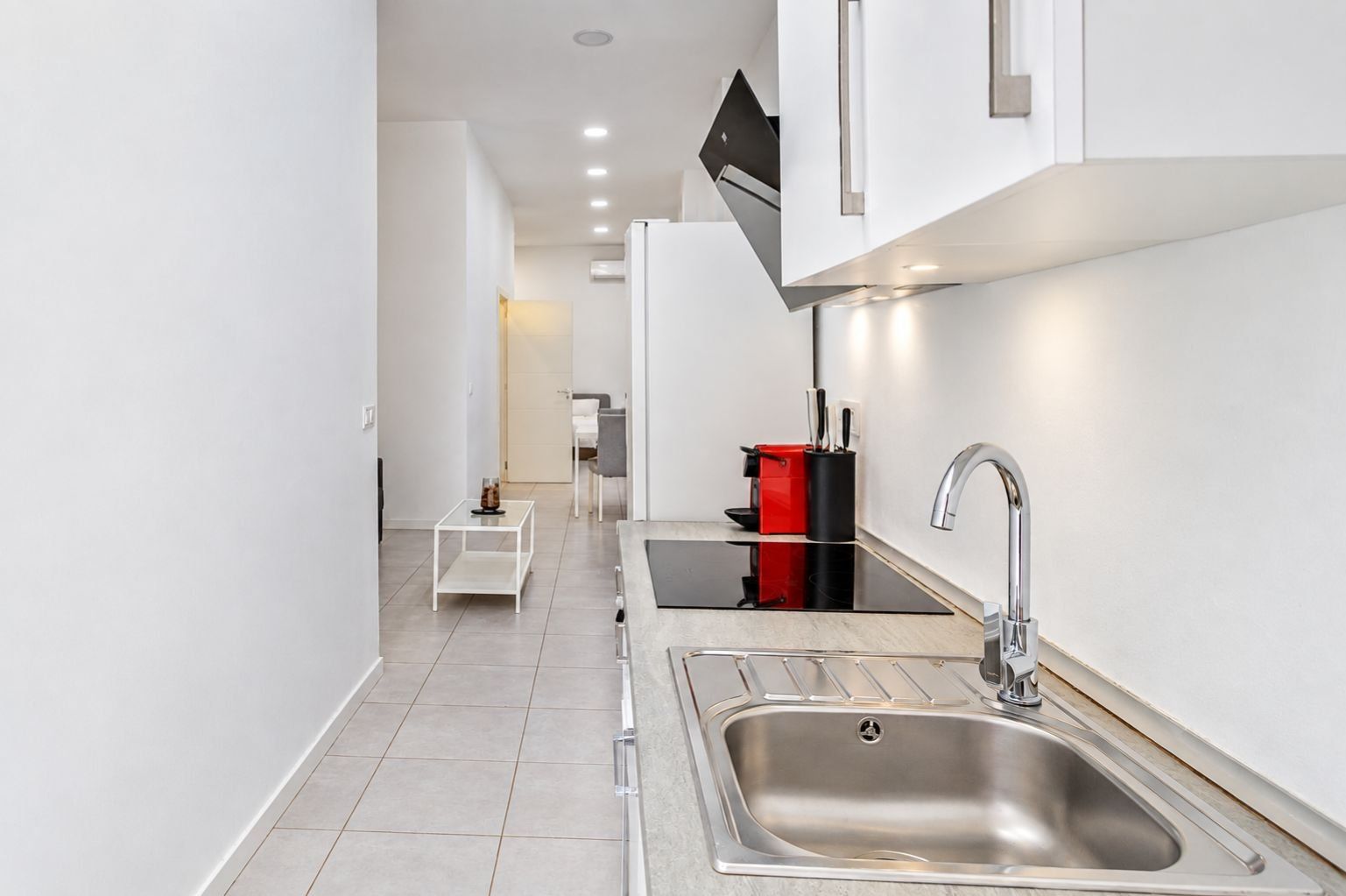Een moderne keuken met een roestvrijstalen spoelbak, een opbergunit in rood en zwart, en een witte tafel met een glazen blad.