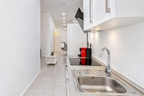 A modern kitchen with a stainless steel sink, a red and black storage unit, and a white table with a glass top. - GuestReady - Cosy studio in Malaga centre (Málaga)