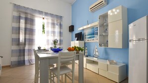 Una cuina amb taula blanca, cadires, un bol blau i nevera blanca.