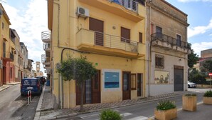 Un edifici groc amb un balcó, una porta i un cartell a la paret.