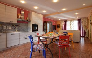 Une cuisine moderne avec un coin repas, comprenant un sol carrelé, une table à manger avec des chaises colorées et un canapé dans le salon.