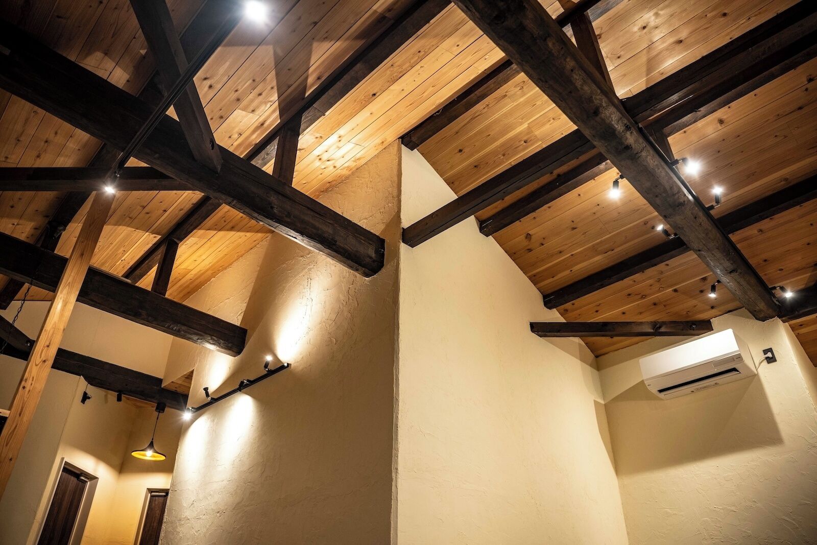 A room with exposed wooden beams, a sloped ceiling, and a wall-mounted air conditioning unit.