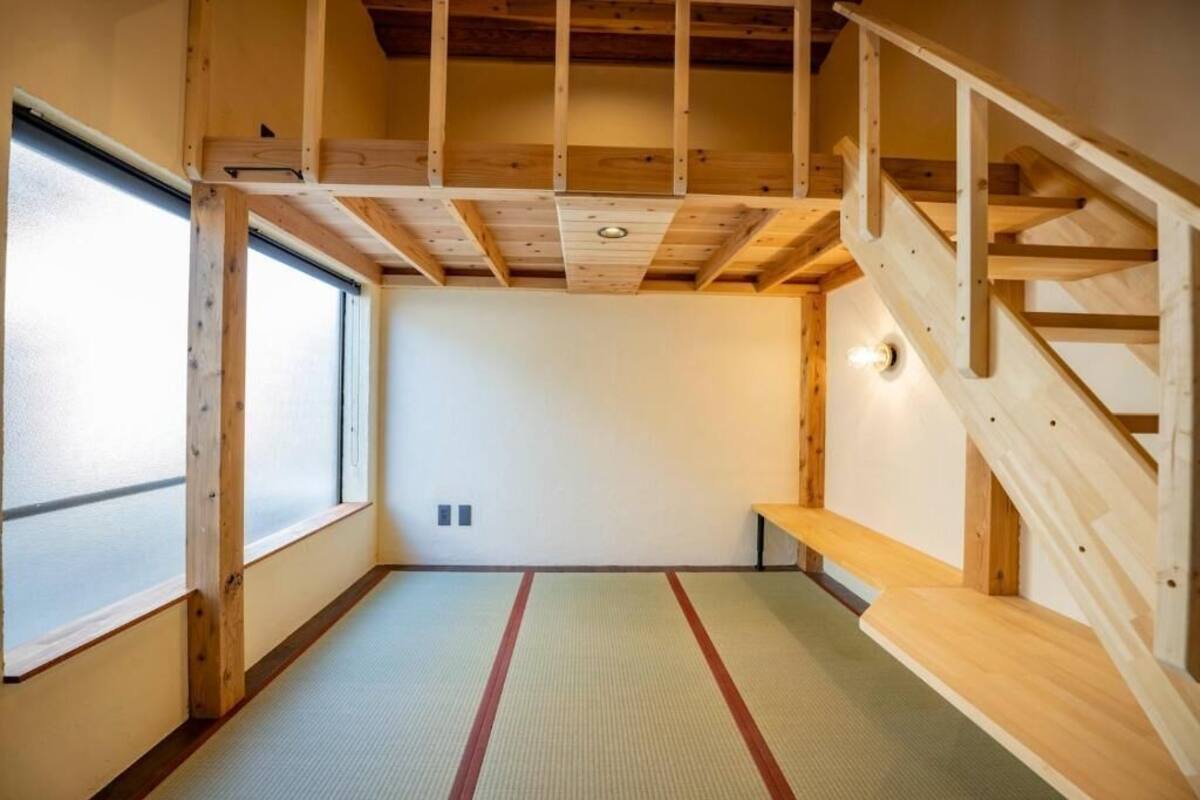 A room with a tatami mat floor, a wooden staircase, and a large window.