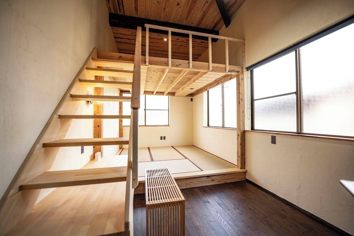 A room with a wooden staircase, tatami mat flooring, and large windows.