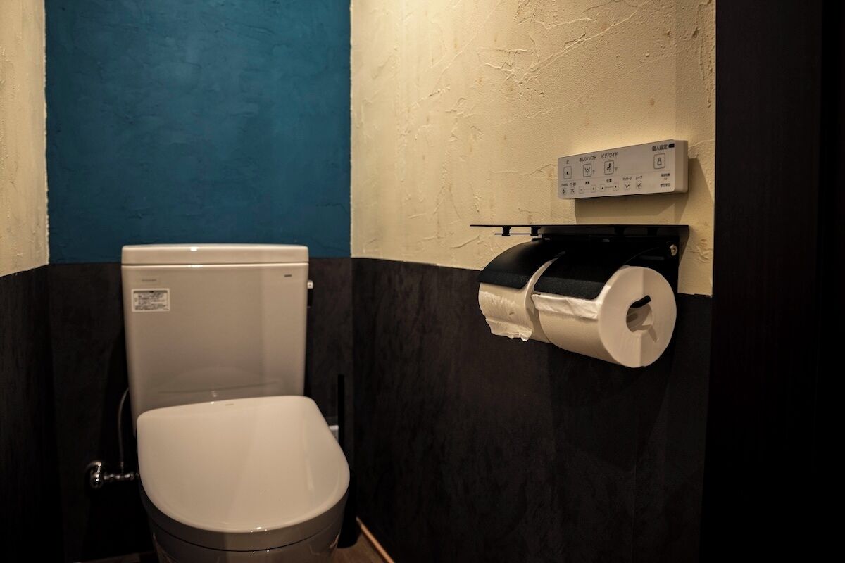A toilet with a paper towel dispenser and a wall-mounted control panel.