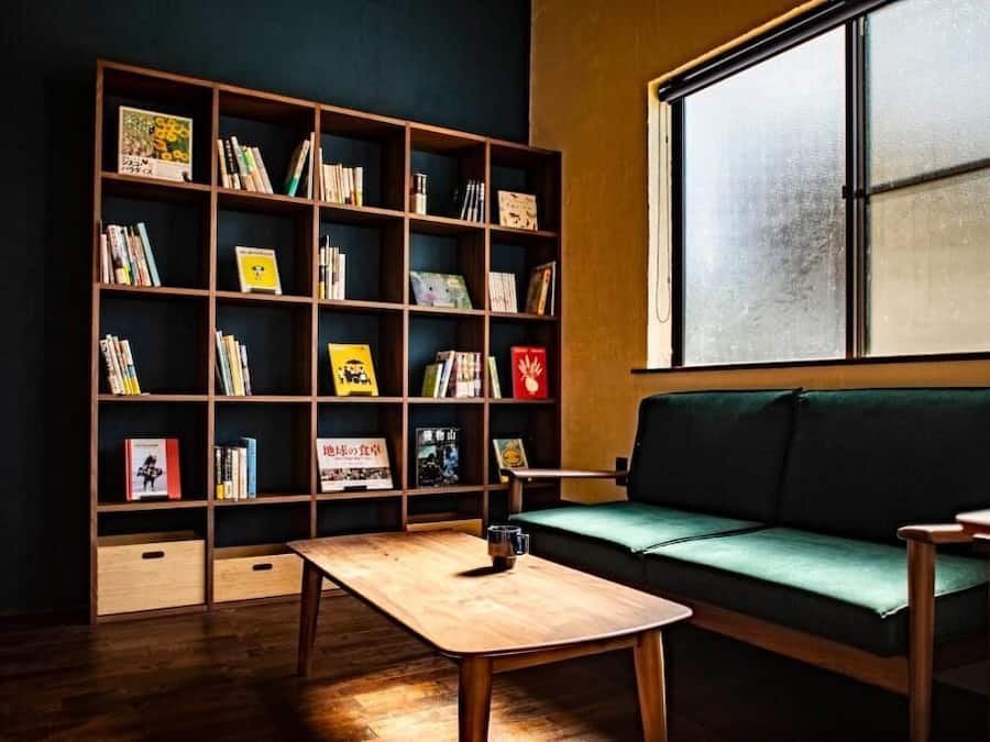 Un coin lecture confortable avec une bibliothèque, un canapé vert et une table en bois.