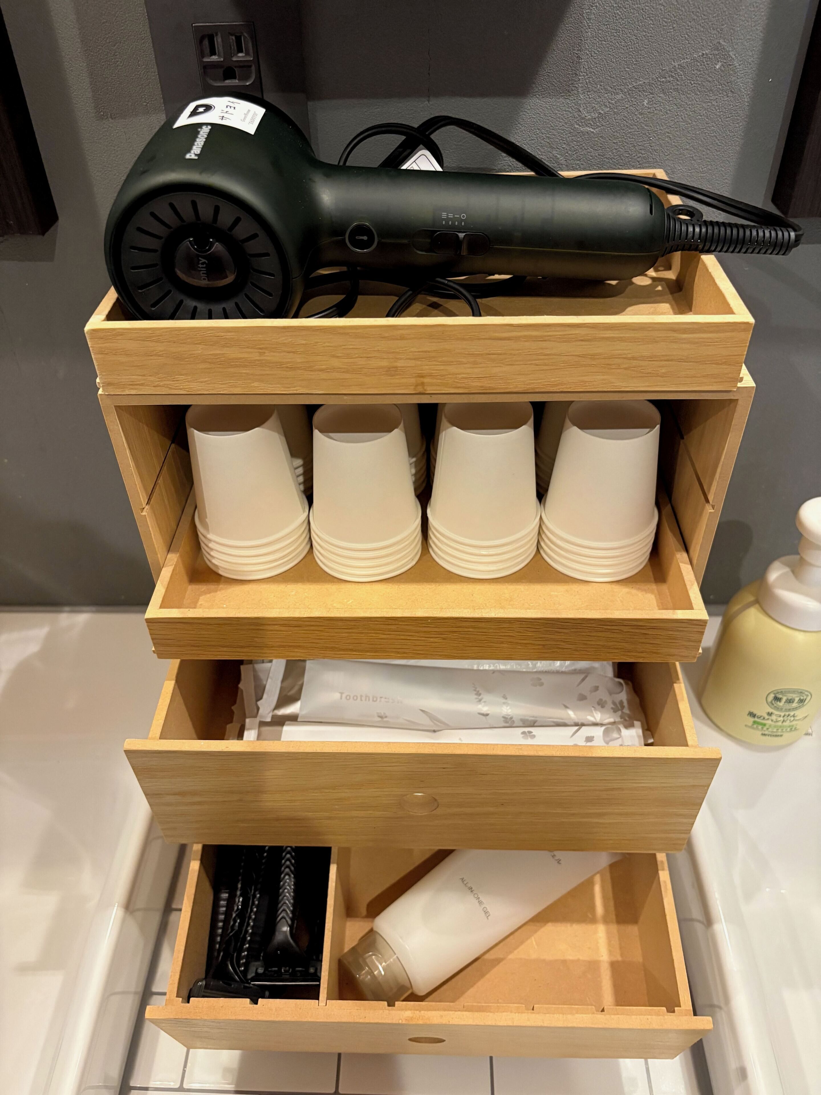 A wooden storage unit with a hair dryer and multiple cups.