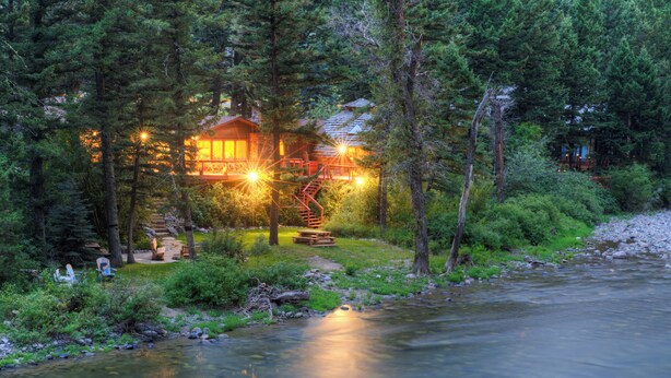 A cabin with a wooden exterior, surrounded by dense forest, near a flowing river. - Riverfront Home, Private Hot Tub, Go Fish! (Gallatin Gateway)