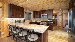 A spacious kitchen with wooden cabinets, a large island with bar stools, stainless steel appliances, and a wooden ceiling. - Riverfront Home, Private Hot Tub, Go Fish! (Gallatin Gateway)
