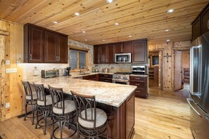 A spacious kitchen with wooden cabinets, a large island with bar stools, stainless steel appliances, and a wooden ceiling. - Riverfront Home, Private Hot Tub, Go Fish! (Gallatin Gateway)