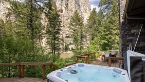 A hot tub on a wooden deck with a view of a rocky cliff and trees. - Riverfront Home, Private Hot Tub, Go Fish! (Gallatin Gateway)
