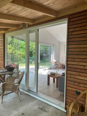 A room with a sliding glass door leading to a patio, wicker furniture, and a small table with a bowl and vase. - Cozy wooden hut with terrace on the Aller. Pet friendly! (Hülsen)