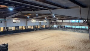 Eine überdachte Halle mit einer Erddbodenfläche, Metallträgern und einem Zuschauerbereich.