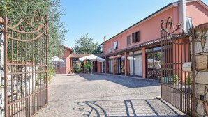 Een omheind erf met een geplaveid pad dat leidt naar een gebouw met grote ramen en een overdekt terras.