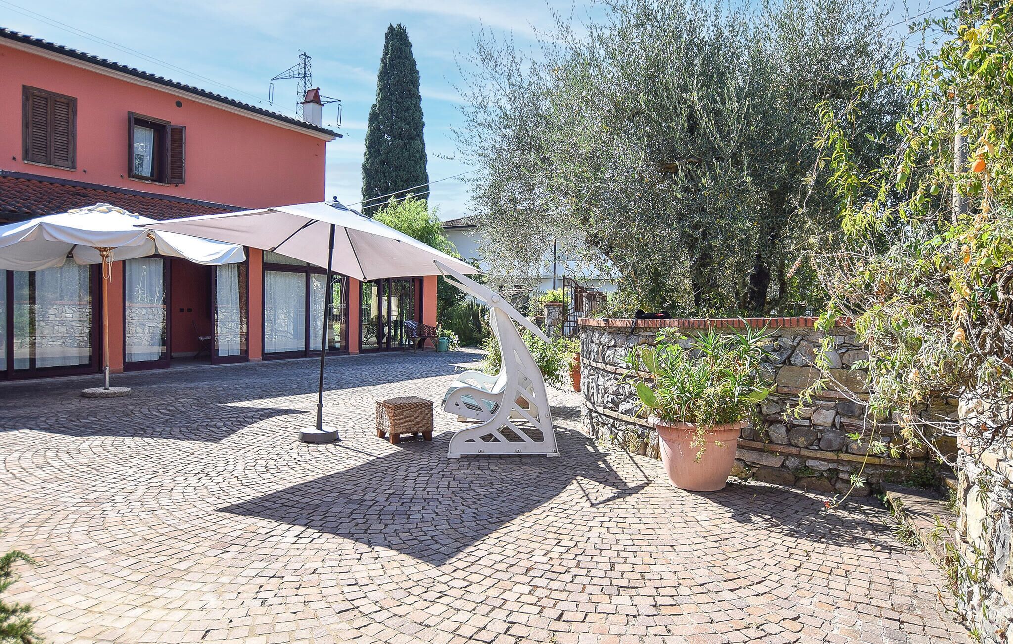 A cobblestone courtyard with outdoor seating, a stone wall, and a building with a red facade.