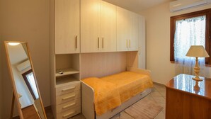 Een kleine slaapkamer met een bed, een kledingkast, een spiegel en een bureau met een lamp.