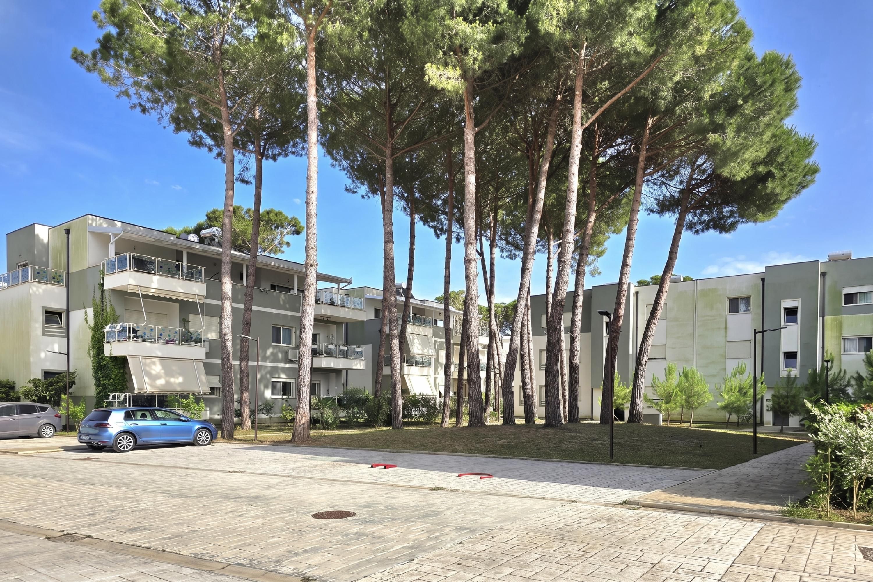 Un immeuble résidentiel doté de nombreux balcons, d’une allée pavée et d’une voiture bleue garée devant.